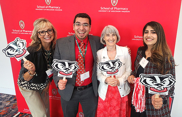 Professors Beth Martin, Ed Portillo, Mara Kieser, and former resident pose together holding Pharmacy Badger signs