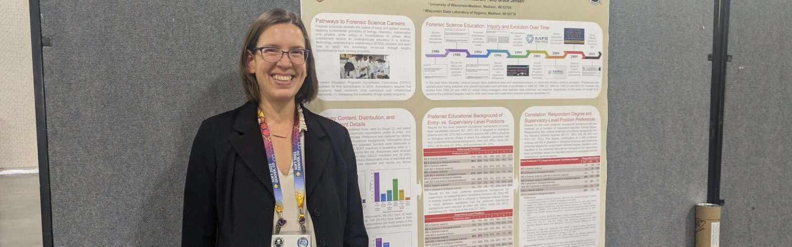 Image of Heather Barkholtz standing in front of a poster presentation at a national conference