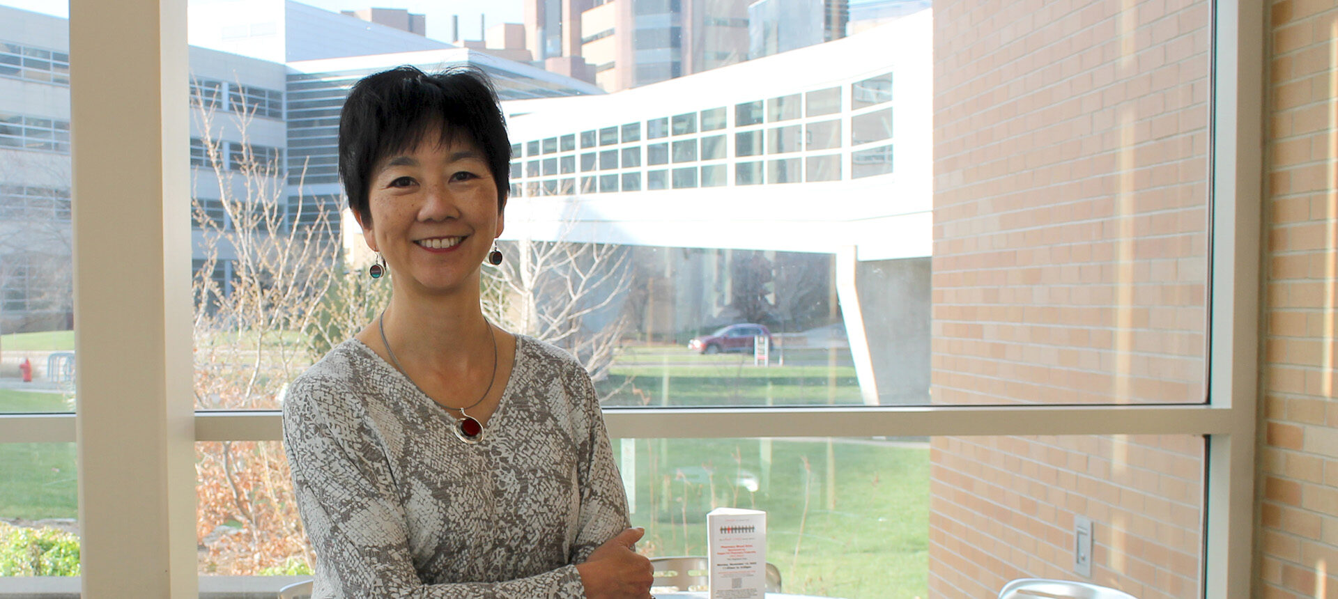 Michelle Chui stands in the School of Pharmacy Mezzanine, with the UW Hospital visible in the background