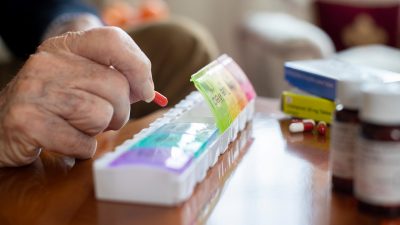 elderly hands putting pills into pill organizer