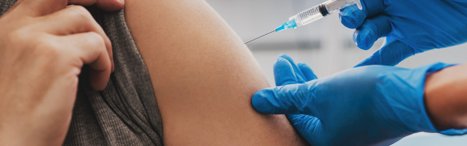 gloved hands giving a patient an injection in bicept