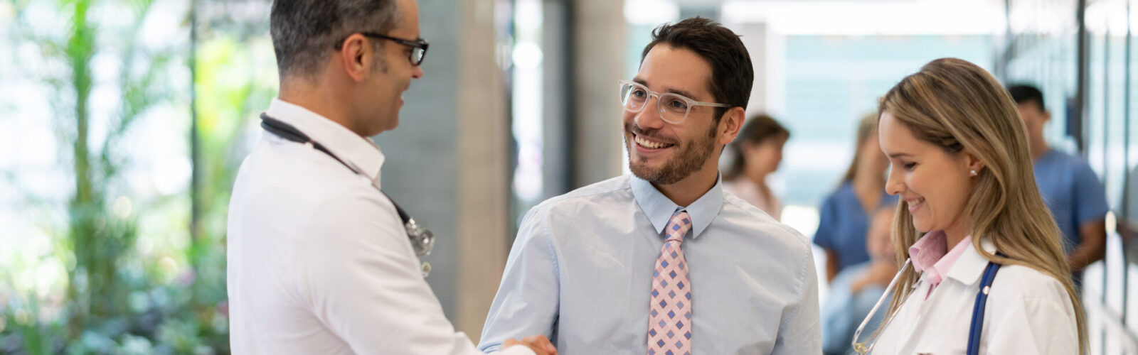male doctor and male shaking hands while female doctor is holding documents