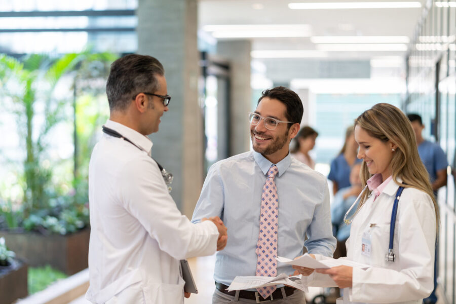 male doctor and male shaking hands while female doctor is holding documents