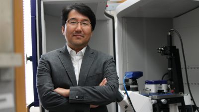 Seungpyo Hong standing with arms-crossed next to an AFM machine in a pharmaceutical lab