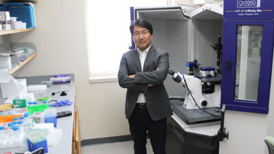 Dr. Hong standing professionally with arms crossed in a lab