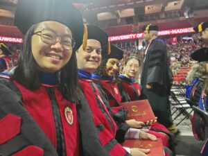 Jiang Research members taking a selfie in their seats with their caps and gowns on Jinshan, Connor, Arielis and Jiaoyang during UW campus commencement.