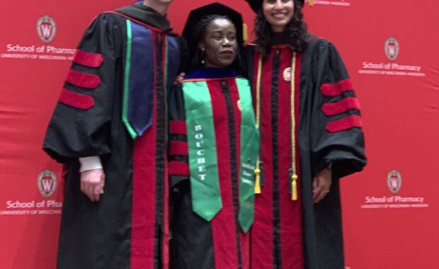 Prof. Shiyanbola posing with Luke Schwerer and Nassim Sarkarati in graduation caps and gowns