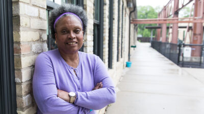 Prof. Eva Vivian posing with arms-crossed against a brick building