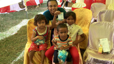 Prof. Eva Vivian in a large tent with Cambodian children holding goodie bags
