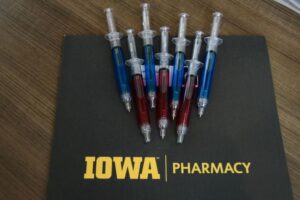 pens designed like syringes laid on top of a black mat labeled IOWA Pharmacy