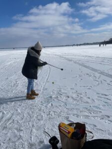 Student in winter-wear hitting a tennis ball with a golf club on a frozen over lake mendota