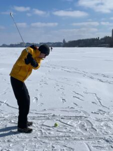 Cody Wenthur on a frozen lake Mendota swinging a golf club at a tennis ball