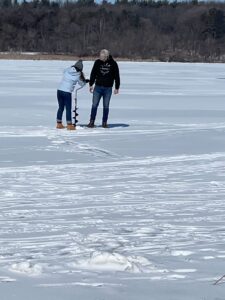 Two students using an auger to drill through the ice on Lake Mendota