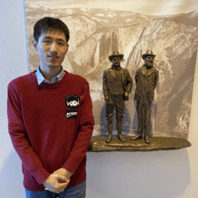 Hao Wu standing in front of a bronze sculpture of two men