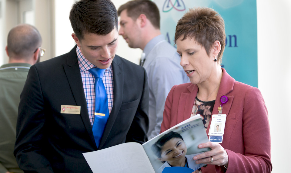 A pharmacy representative at the annual career fair shares information in a booklet with a PharmD student