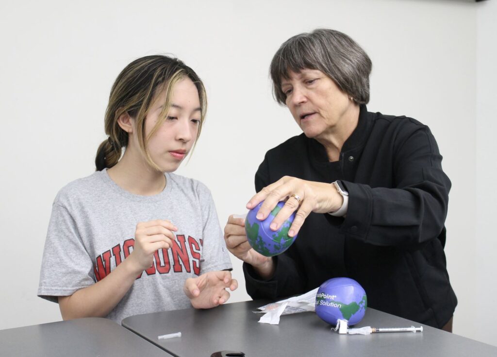 Professor Mary Hayney demonstrates proper syringe injection technique to a student