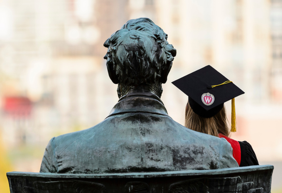 A student in graduation robe sits on the statue of Abraham Lincoln