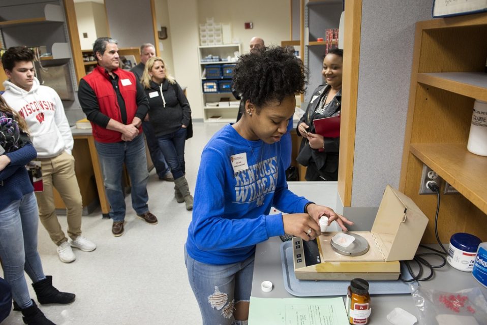 A high school student weighs medication on a scale before adding it to a mixture for a lotion.