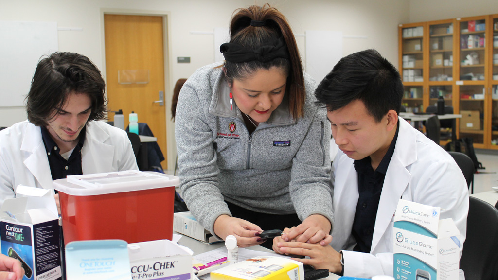 Professor Marina Maes assists a second-year Pharmacy student with using a glucometer in a Diabetes lab class.