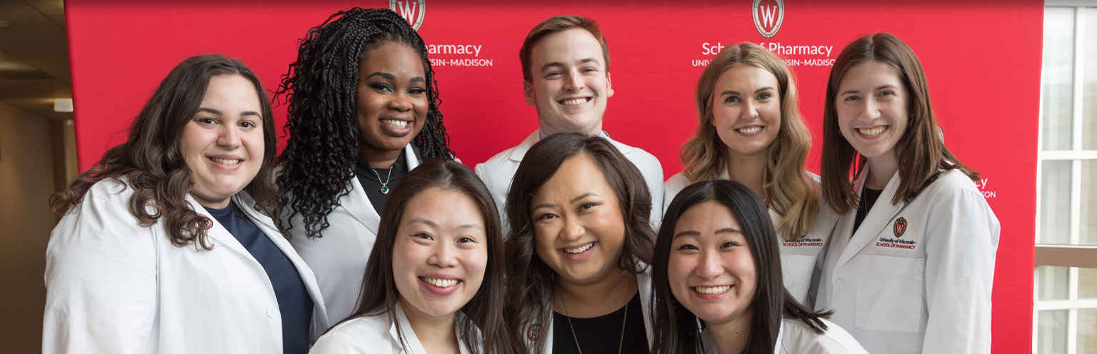 Eight PharmD students pose together with big smiles following the white coat ceremony