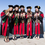 A group of graduates in robes hold up W hands