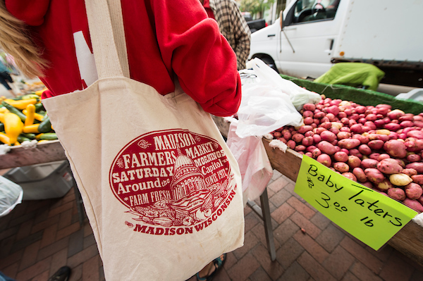 Pedestrians shop for fresh potatoes and other produce while walking around the Dane County Farmers' Market that circles the Wisconsin State Capitol in downtown Madison, Wis., during a spring morning on June 20, 2015. Attending the Farmers' Market is a favorite weekend activity for many University of Wisconsin-Madison students and members of the Madison community. (Photo by Jeff Miller/UW-Madison)