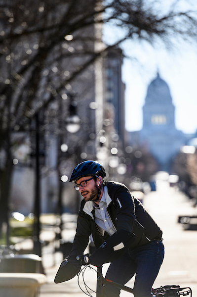 University Communications science writer Eric Hamilton bikes along State Street and Library Malls as he commutes to work at the University of Wisconsin-Madison during a spring morning on April 9, 2019. In the background is the dome of the Wisconsin State Capitol. (Photo by Jeff Miller / UW-Madison)