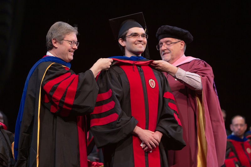 Professors Chuck Lauhon (left) and Melgardt de Villiers straighten the hood on Class of 2019 Pharmsci graduate Pawel. Photo by Todd Brown, Media Solutions.