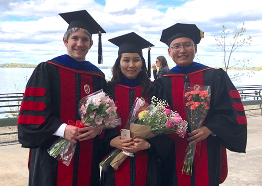 SAS graduates pose with bouquets in front of the lake following commencement.