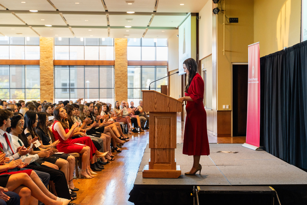 PharmD student Jennifer Velikodanov speaks at the podium in front of the applauding class.