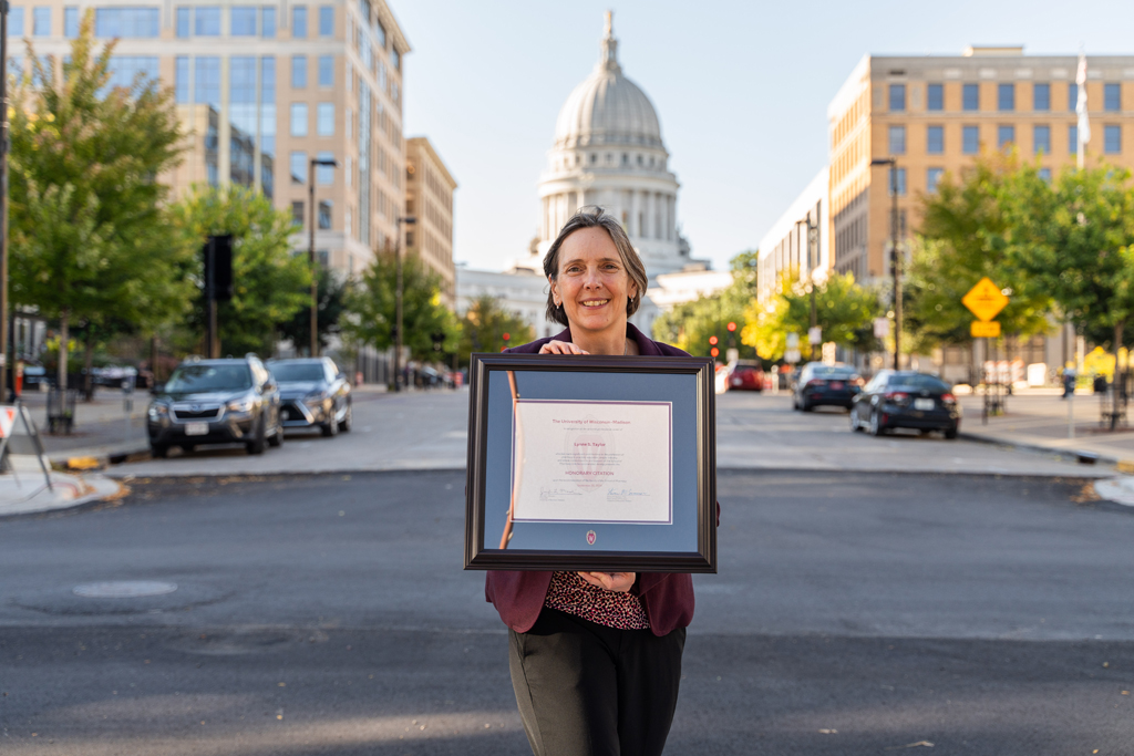 Lynne Taylor holds her award with the Wisconsin capitol building behind her