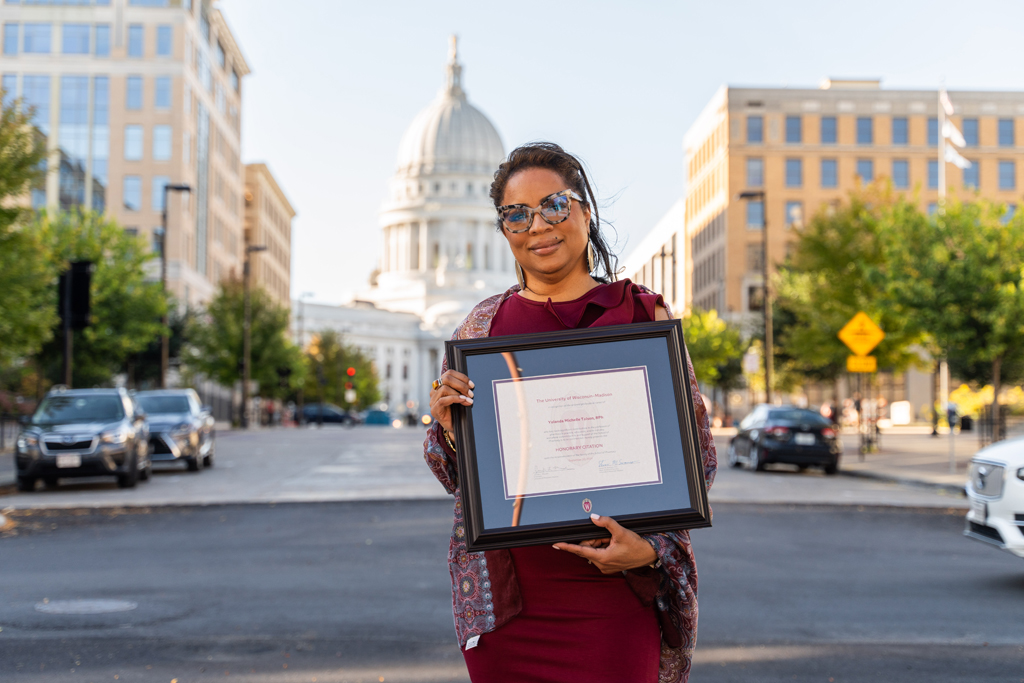 Yolanda Tolson holds her award with the Wisconsin capitol building behind her