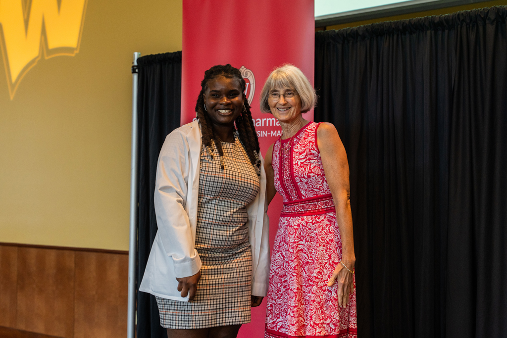 A student poses with Mara Kieser in front of a red School of Pharmacy banner