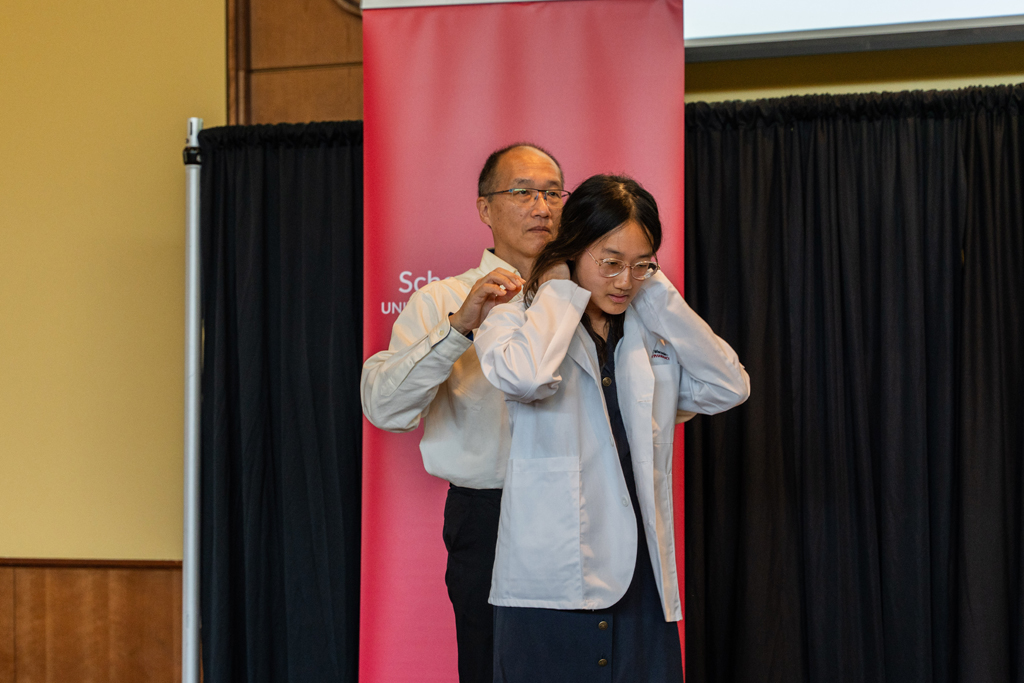 A student receives her white coat from an older man