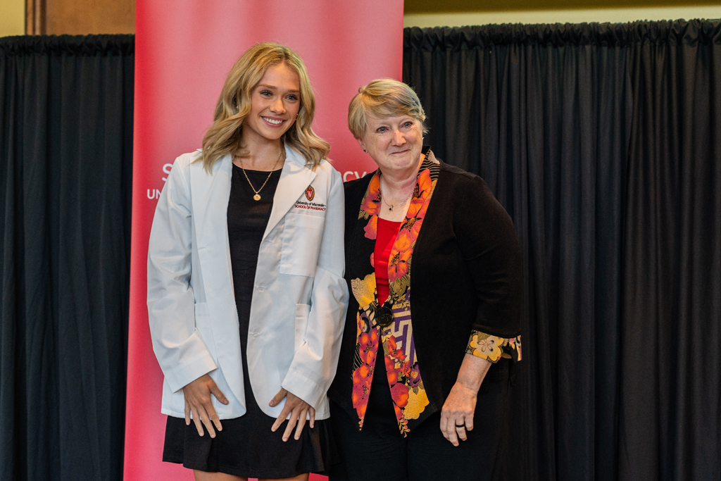 A student poses with karen Kopacek in front of a red School of Pharmacy banner