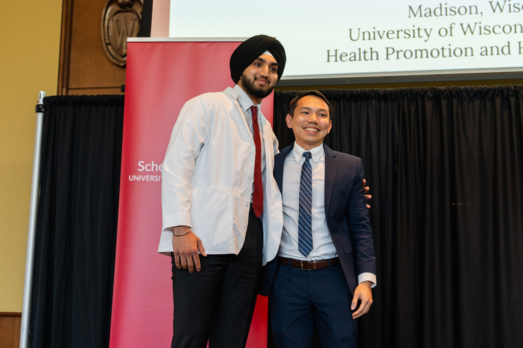 A student poses with Sean Lim in front of a red School of Pharmacy banner