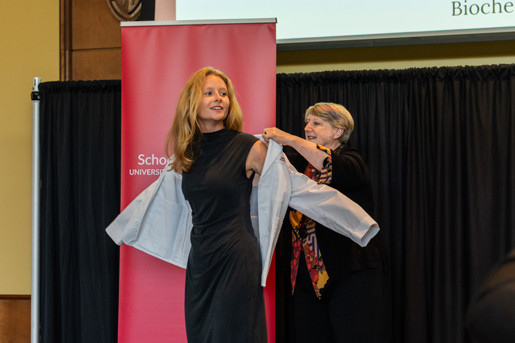 A student receives her white coat from Karen Kopacek