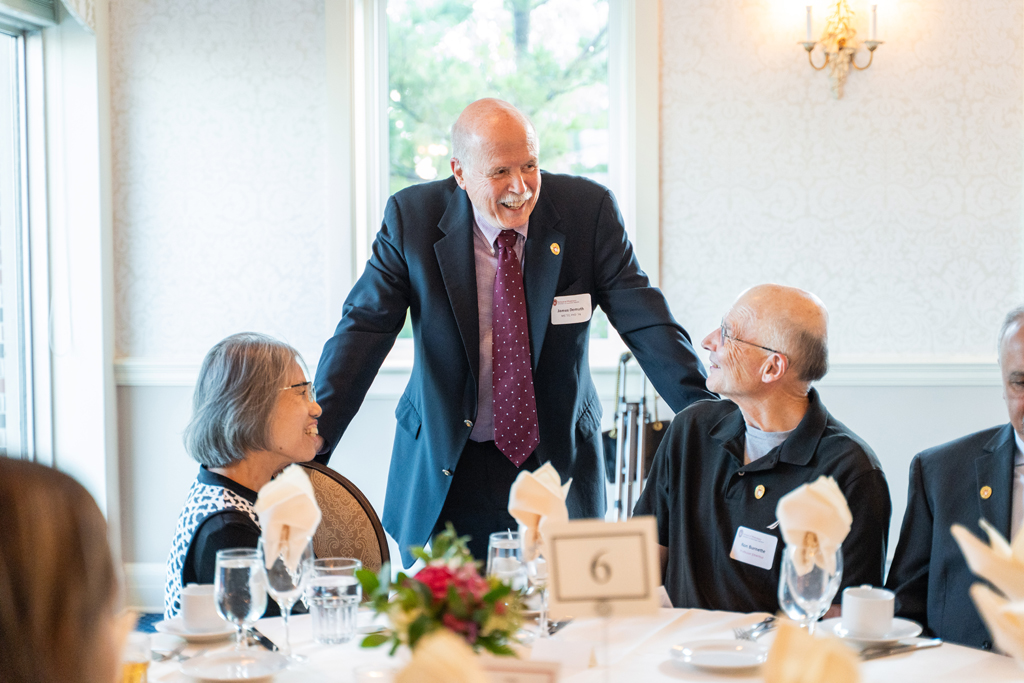 John DeMuth speaks with two seated attendees, including Ron Burnette