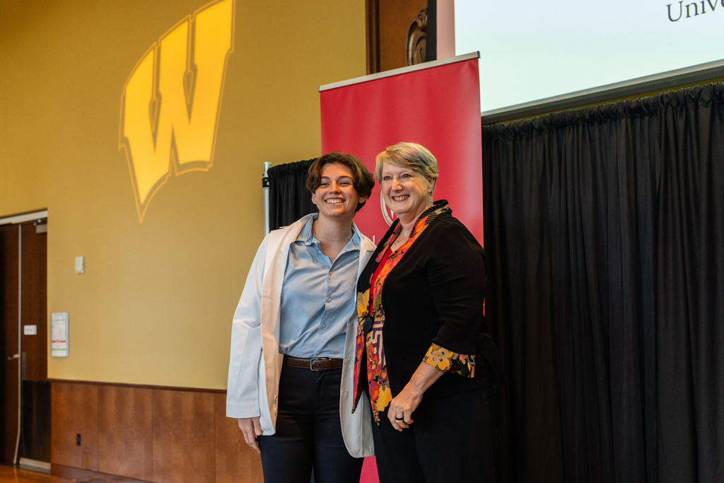 A student poses with Karen Kopacek in front of red School of Pharmacy banner