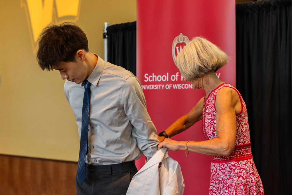 A student receives his white coat from Mara Kieser