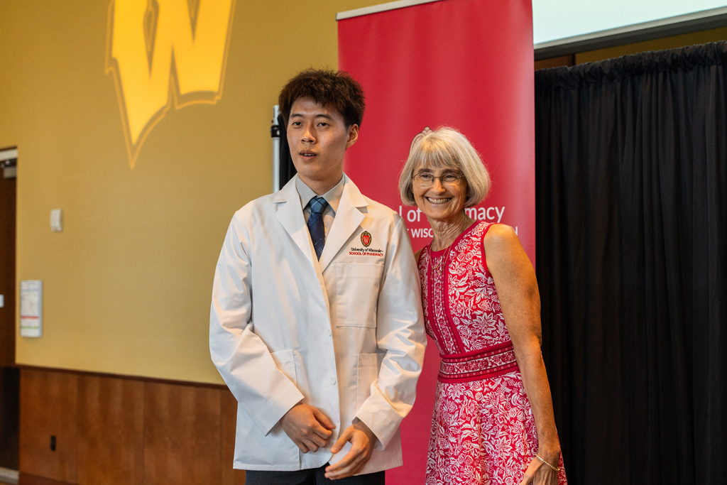 A student poses with Mara Kieser in front of a red School of Pharmacy banner