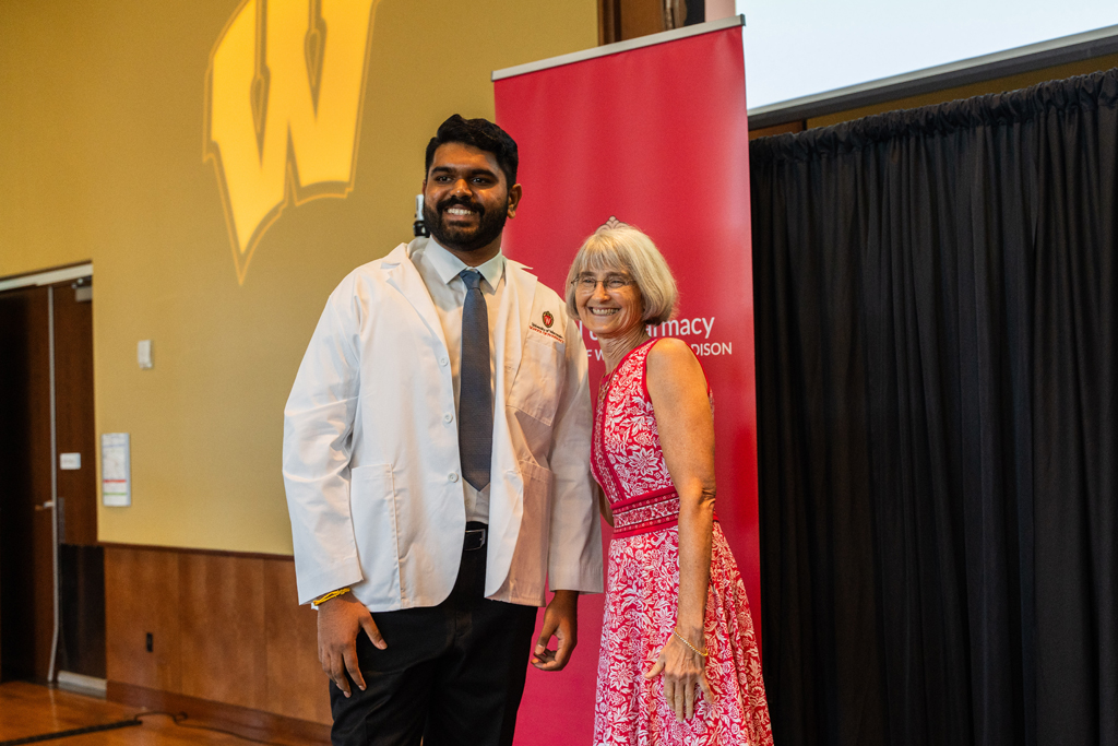 A student poses with Mara Kieser in front of a red School of Pharmacy banner