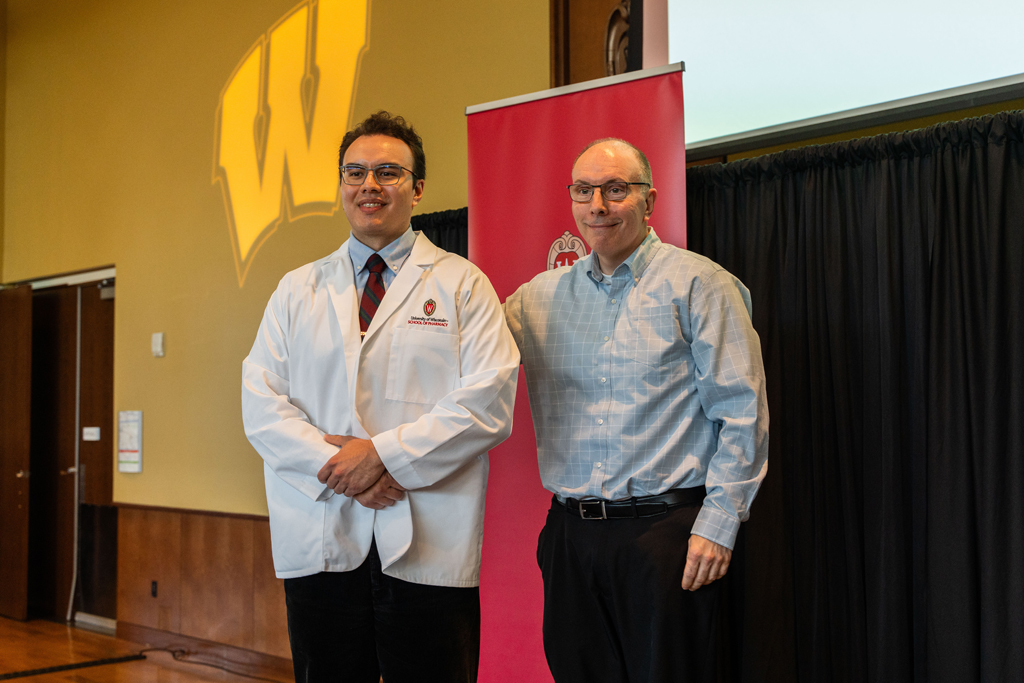 A student poses in front of a red School of Pharmacy banner with an older man