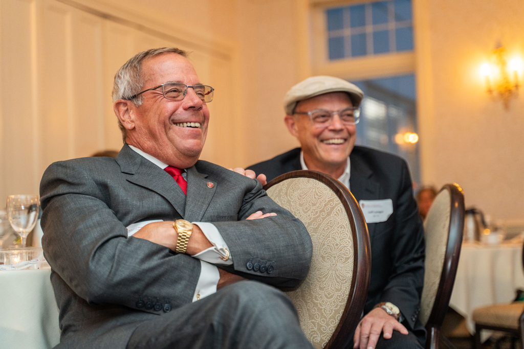 Two seated men are laughing while listening to a speaker.