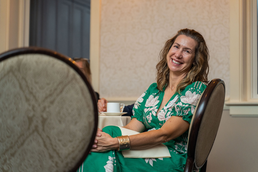 A woman in a floral dress sits at a table and smiles