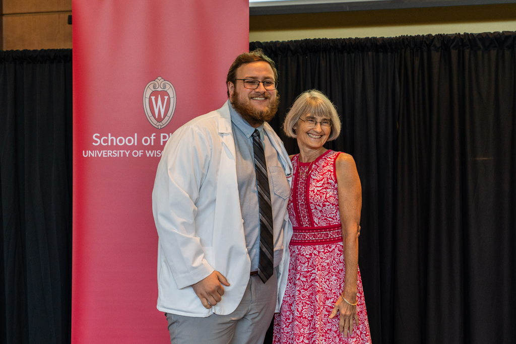 A student poses with Mara Kieser in front of a red School of Pharmacy banner