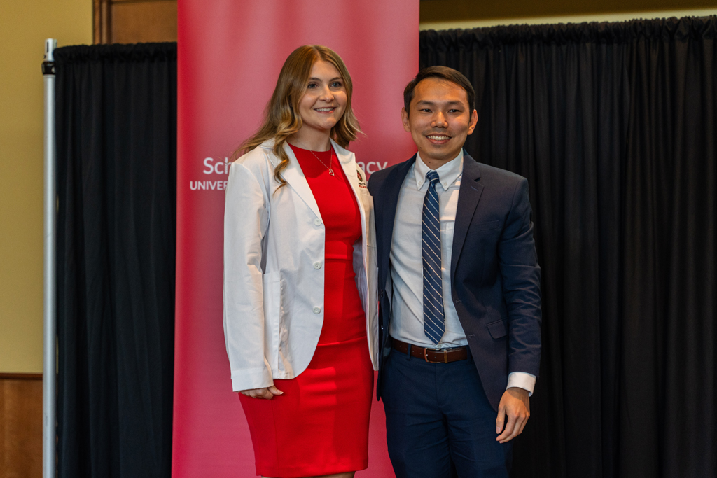 A student poses with Sean Lim in front of a red School of Pharmacy banner