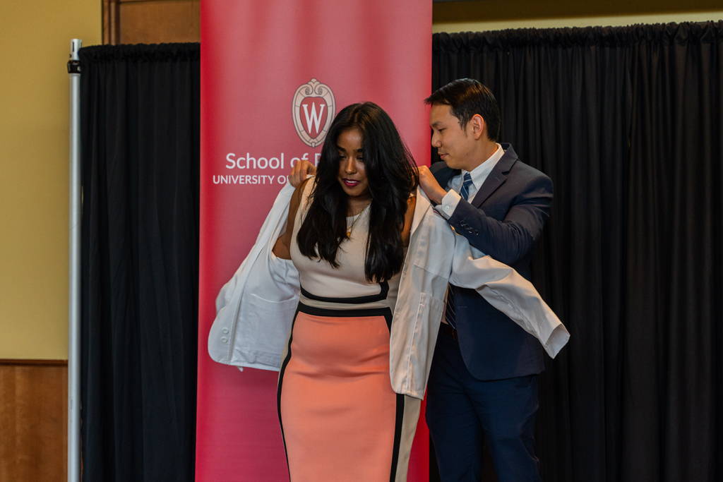 A student receives her white coat from Sean Lim