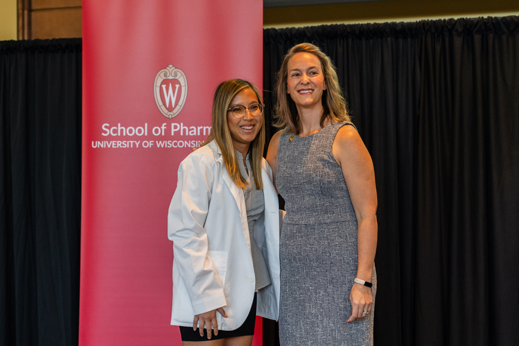 A student poses with Kate Rotzenberg in front of the red School of Pharmacy banner