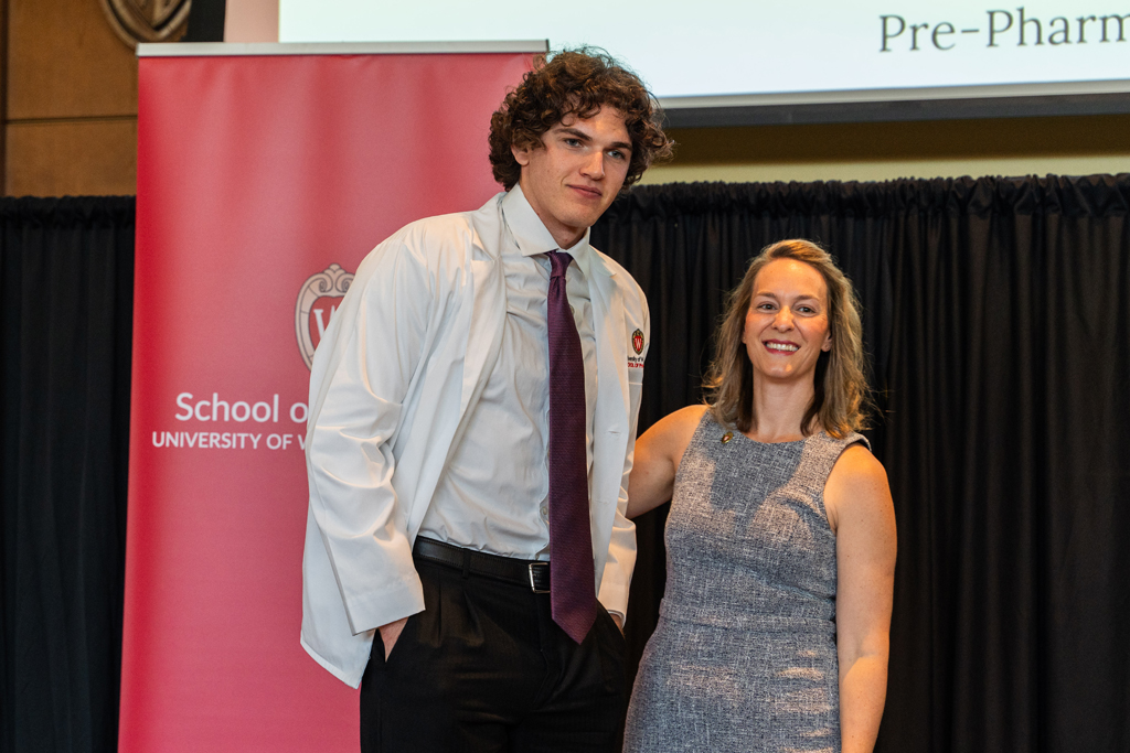 A student poses with Kate Rotzenberg in front of the red School of Pharmacy banner